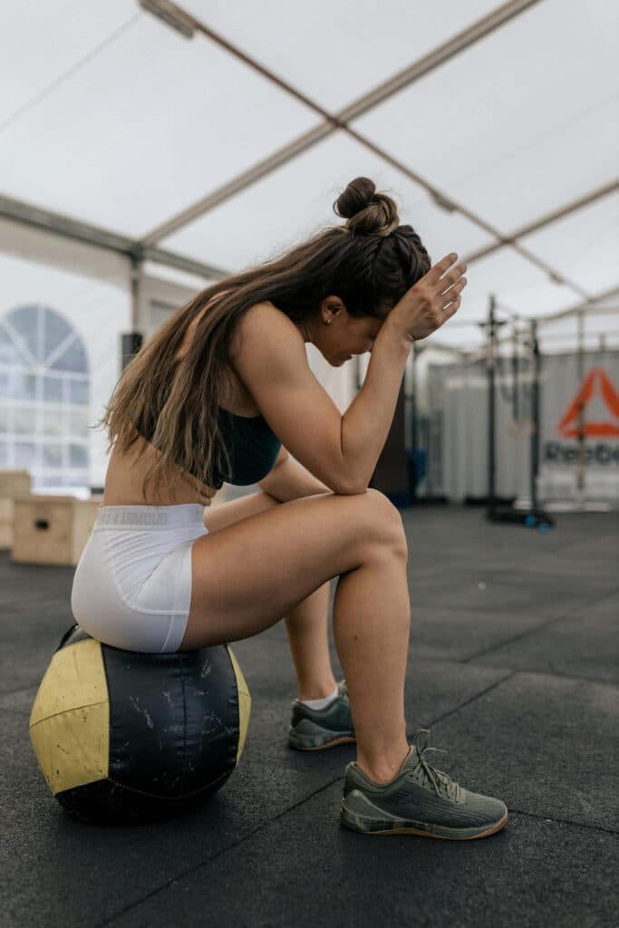 Girl in a gym sitting on a workout ball with her elbows on her knees looking exhausted from being always in season.