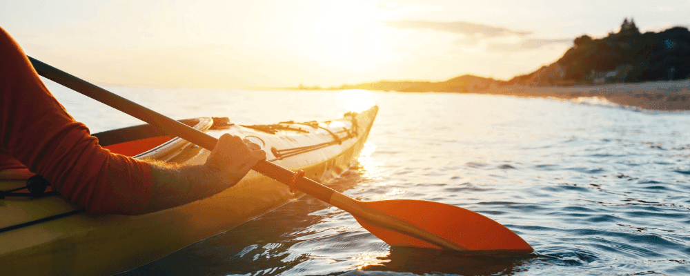 View of a man kayaking near the shore at sunset.
