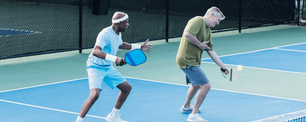 Two men playing pickleball on an outdoor pickleball court and one of the men is holding his elbow in pain.