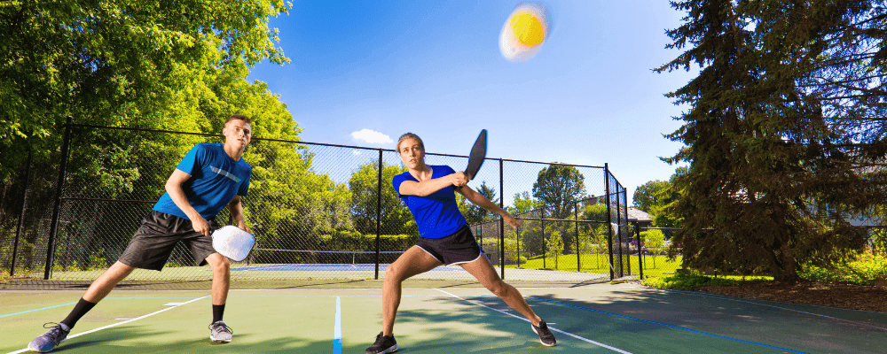 Man and woman at an outdoor pickleball court playing pickleball.