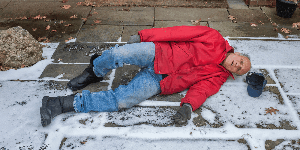 Older man on the snow covered ground outside in pain.