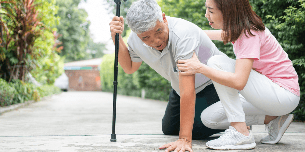 Woman assisting an older man off the floor while he holds onto a walking cane for additional support.