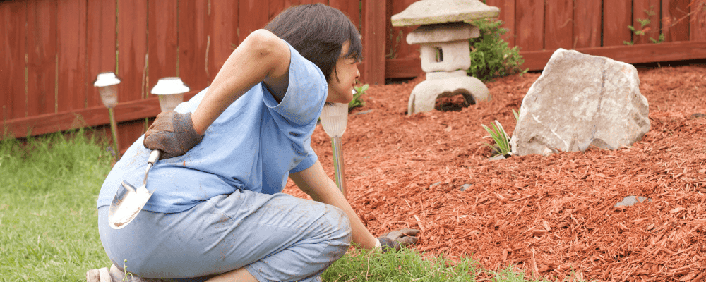 Woman outside gardening, bent down, and holding her low back in pain.