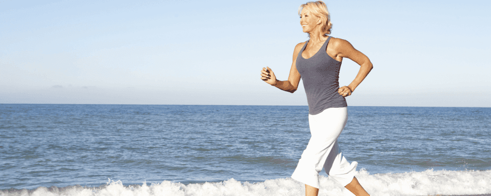 Older fit woman running on the beach.