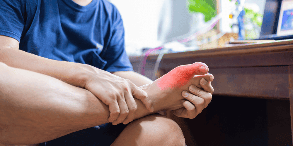 Man sitting in front of his desk holding his foot in pain.