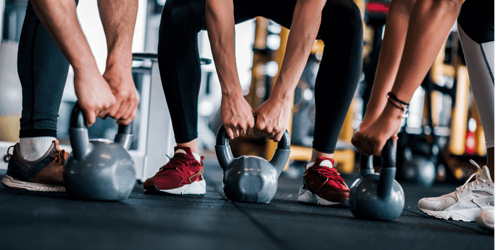 Group of people doing deadlifts with kettlebells.
