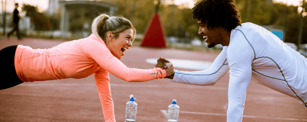 A man and woman doing a plank on one hand outside while holding each other's hand.