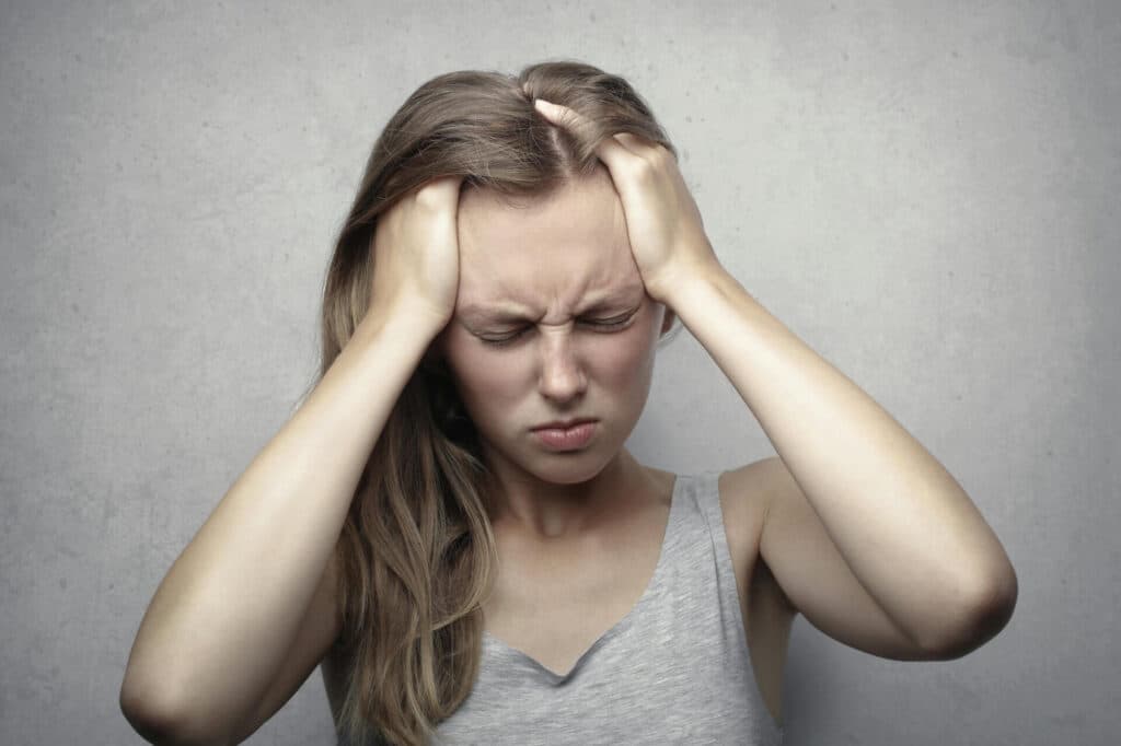 Woman with both hands on her head grimacing in pain due to chronic headaches in Bend. She needs chronic headache relief.