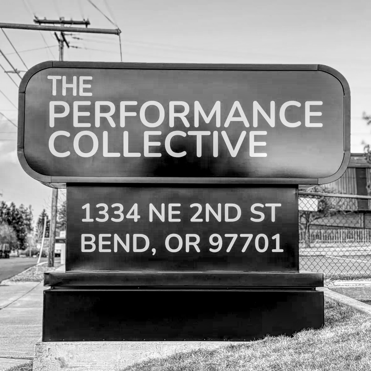 Large black street sign for The Performance Collective, located at 1334 NE 2nd St, Bend, OR 97701. The sign is positioned at the entrance of the parking lot and is visible from the road.